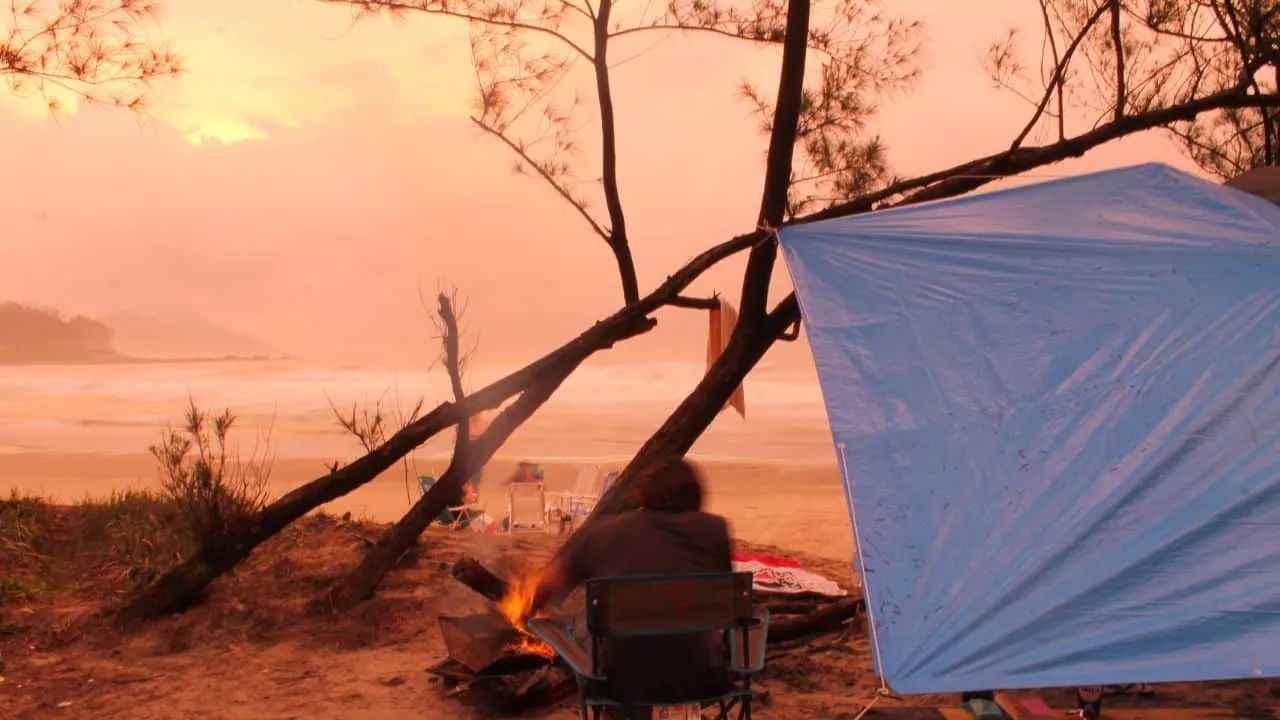 Camper sitting next to a campfire and using a tarp for shelter